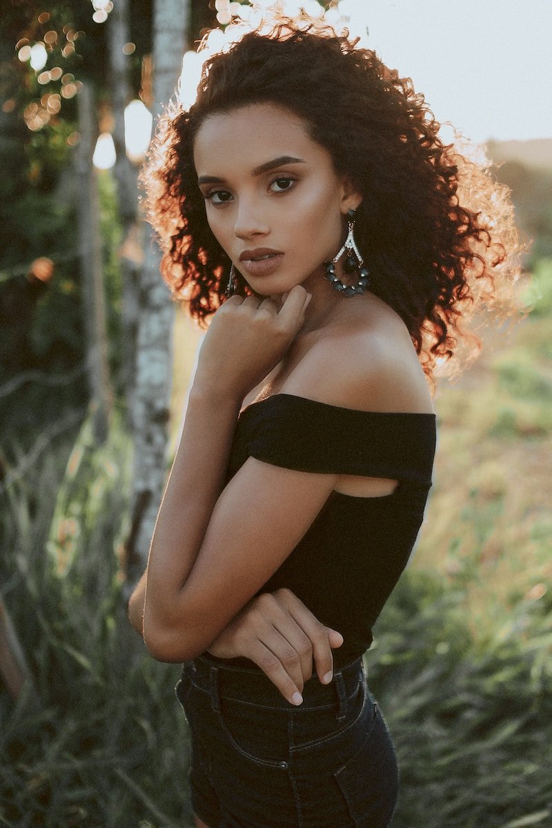 woman wearing black off-shoulder top with left hand under chin during daytime