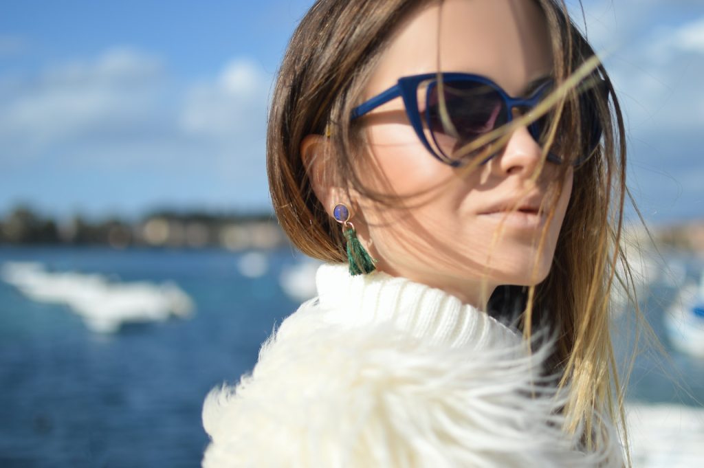 Why Do Earrings Come With Rubber Backs woman wearing blue-framed cat-eye sunglasses with body of water background