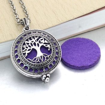 A silver-colored Aroma Essential Oil Diffuser Pendant Necklace with a tree design and purple accents, displayed next to a purple felt pad, perfect for those following the latest women's fashion trends.
