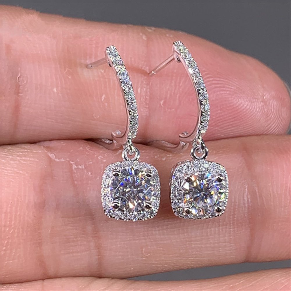 A pair of Women's Crystal Drop Earrings are being held in a hand.