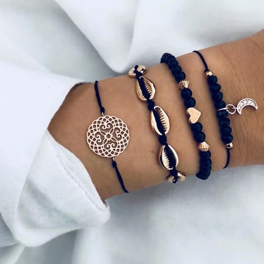 A person's wrist adorned with a collection of Bohemian Rope Chain Bracelets for Women, including beaded and charm designs on a fabric background, showcases the latest fashion trends.