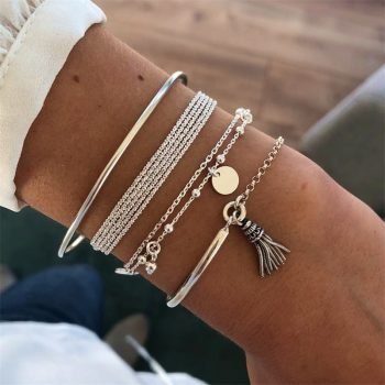 A person's wrist is adorned with a collection of delicate bracelets, a trendy fashion accessory, including beaded, chain, and bangle styles, one featuring a Women's Bohemian Tassel Round Bracelet.