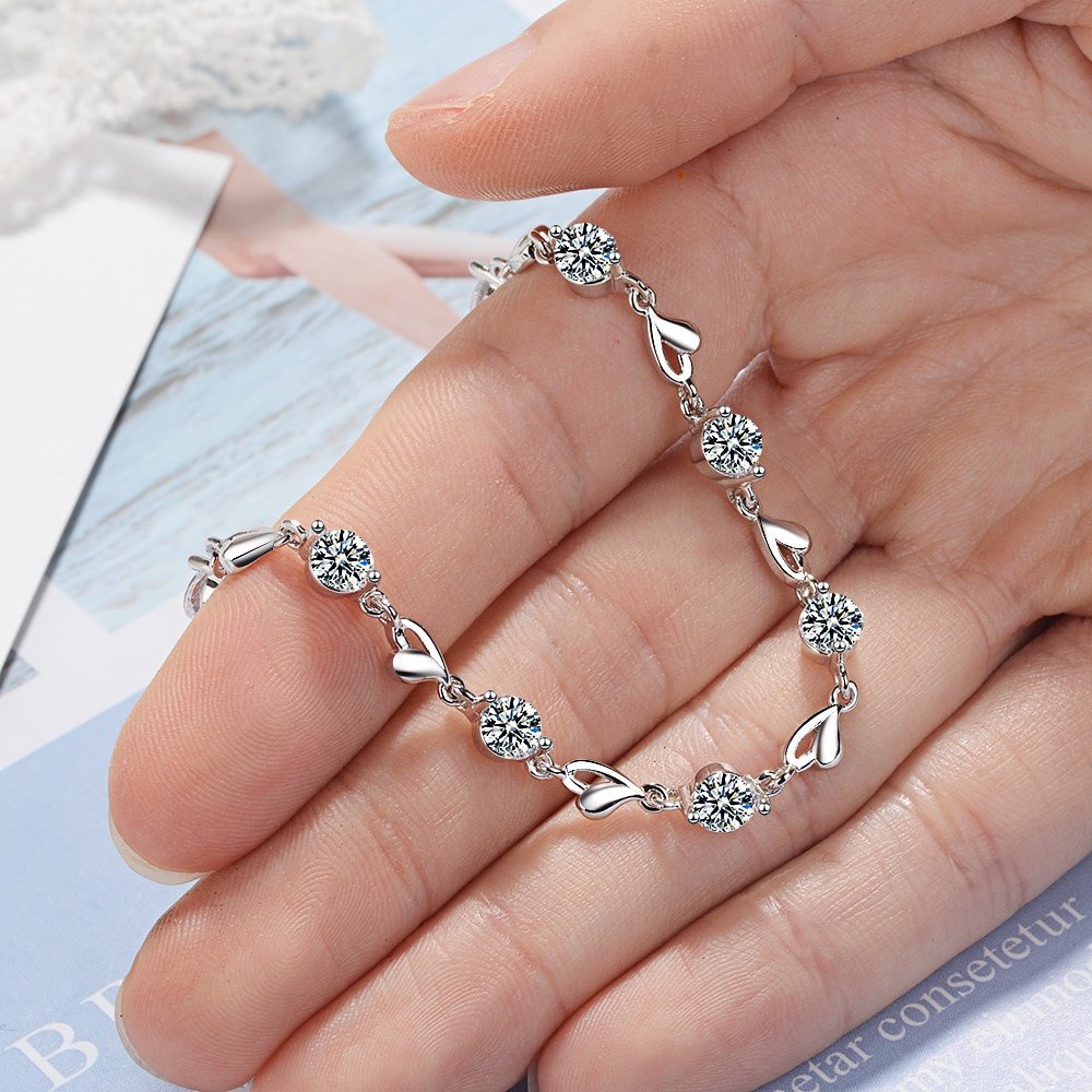A hand displaying a Women's 925 Sterling Silver Zircon Bracelet with hearts design and gemstone accents, embodying new fashion trends as a chic fashion accessory.