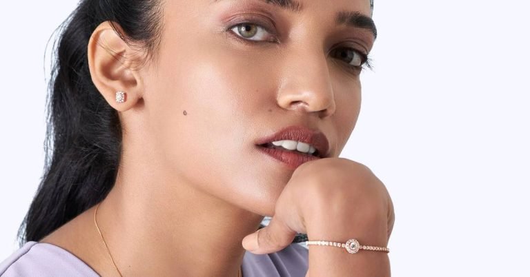 A close-up of a woman with subtle makeup, showcasing new fashion with a diamond earring and a delicate bracelet, posing with her hand resting on her chin.