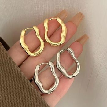 A hand holding four Luxurious Geometric Hoop Earrings for Women, two gold and two silver, against a light background, showcasing a new fashion accessory.