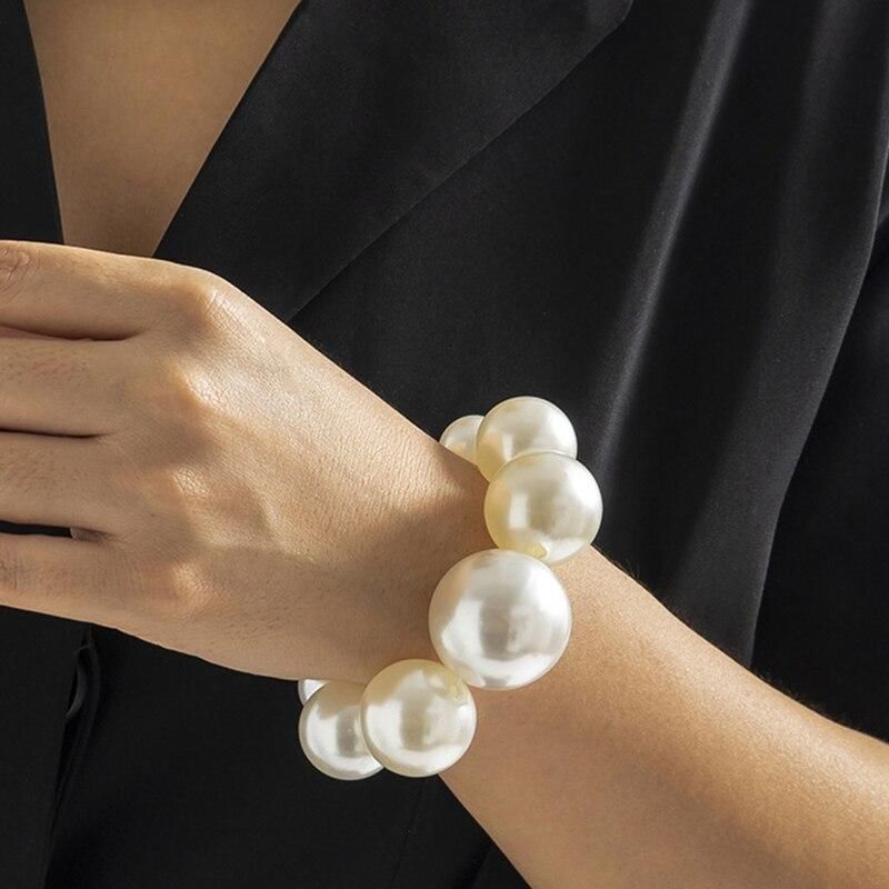 A close-up of a woman's wrist wearing a Womens Round Pearl Charm Bracelet, against a black blazer background, showcasing popular fashion trends.